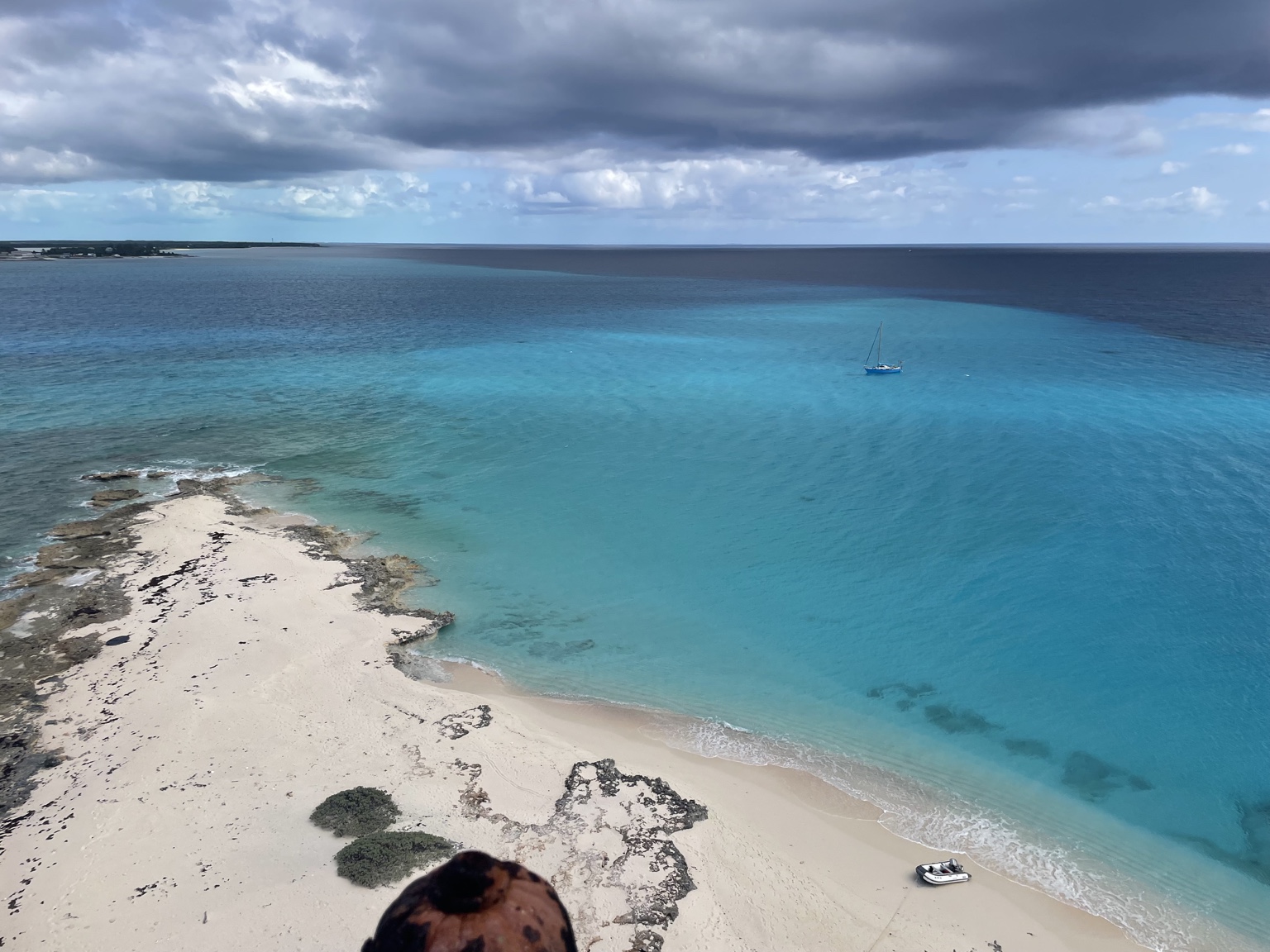 Aerial view of a beach and turquoise water with sailboat nearby